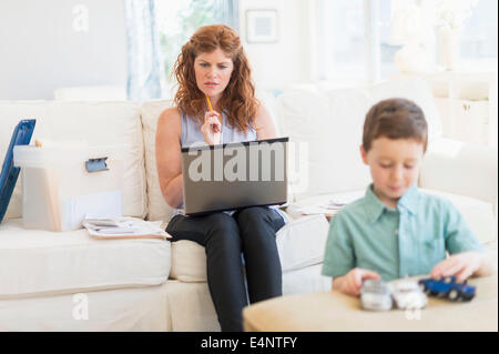 Mother using laptop, son (6-7) playing with toy cars Stock Photo