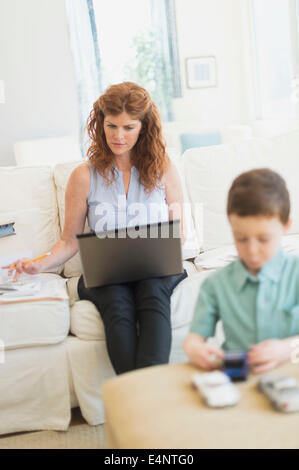 Mother using laptop, son (6-7) playing with toy cars Stock Photo