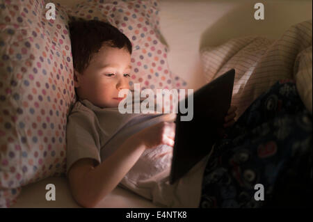 Boy (6-7) using digital tablet in bed Stock Photo