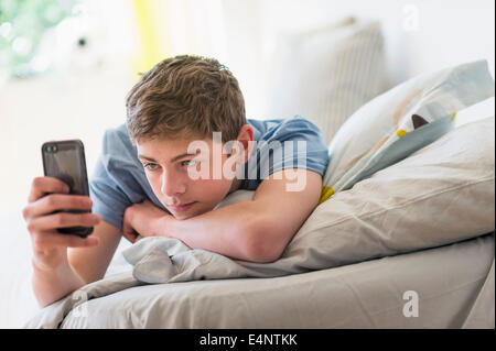 Teenage boy (16-17) lying on bed and text messaging Stock Photo