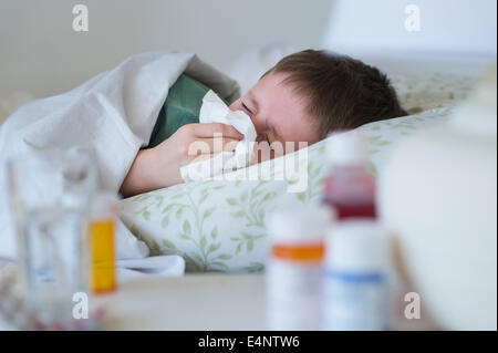 Boy (8-9) lying in bed and blowing nose Stock Photo