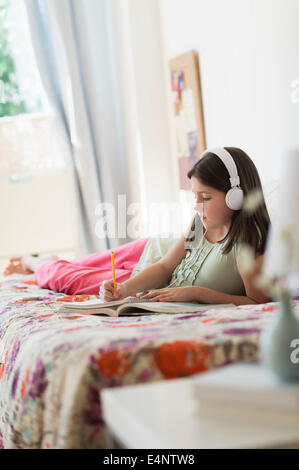 Girl (10-11) lying in bed and learning Stock Photo