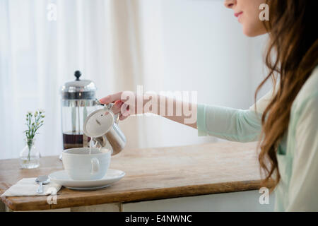 Young woman pouring milk into coffee cup Stock Photo