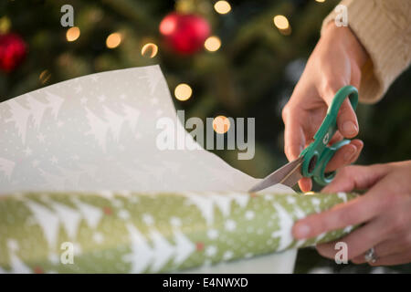 Woman's hands using scissors to cut Christmas wrapping paper Stock
