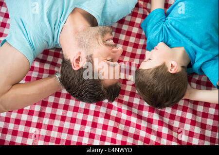 Father and son (8-9) relaxing on checked blanket Stock Photo