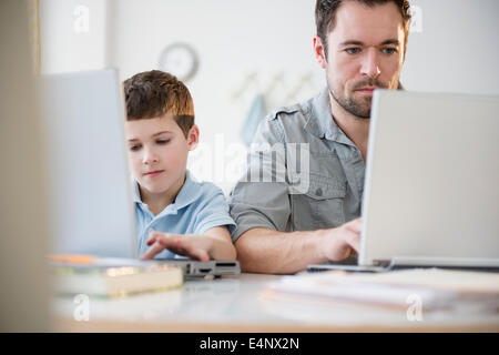 Father and son (8-9) working on laptops Stock Photo