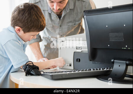 Father and son (8-9) setting up printer with computer on table Stock Photo