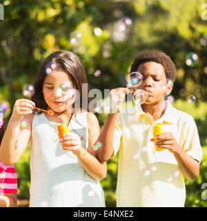 Girls (4-5, 8-9) and boy (6-7) blowing soap bubble Stock Photo