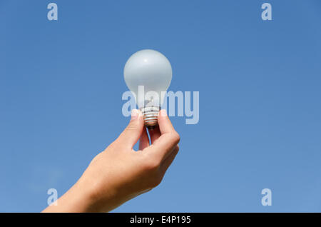 hand holding an incandescent light bulb on blue sky background Stock Photo