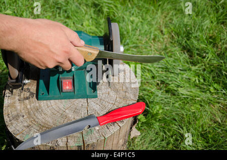 Hand grinder knives with electric tool on outdoor log. Stock Photo