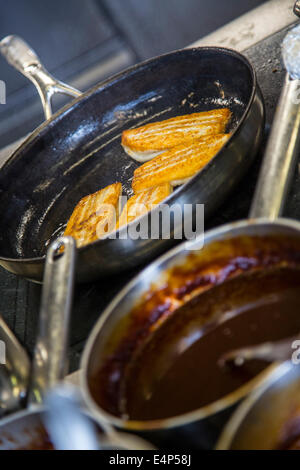 Kitchen of a restaurant, cooking pans and pots on an kitchen stove, fish fillet in a pan Stock Photo