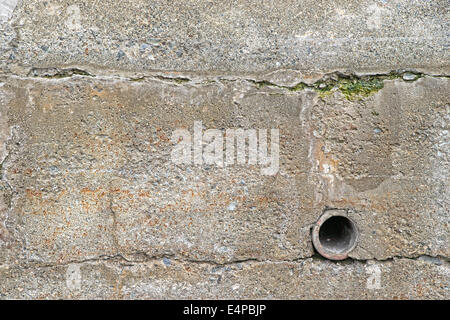 An old exterior retaining wall with a clay drainpipe and surface cracks with algae. Stock Photo