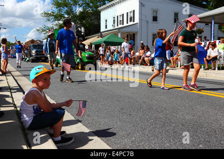 Bored boy sitting on pavement holding America flag during 4th of July Independence Day parades, Catonsville, Maryland, USA Stock Photo