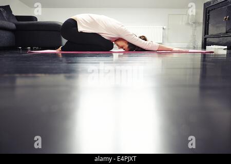 Side view of fit young lady practicing yoga at home. Healthy woman exercising in living room. Stock Photo