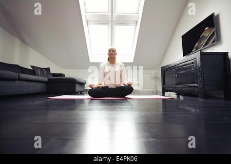 Portrait of healthy young woman exercising yoga in living room. Fitness female relaxing with yoga meditation at home. Stock Photo