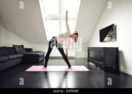 Fit young woman doing stretching exercise at her home. Healthy caucasian female model exercising in living room. Stock Photo