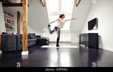 Full length image of fit young lady practicing yoga at home. Healthy young woman exercising in living room. Caucasian model. Stock Photo