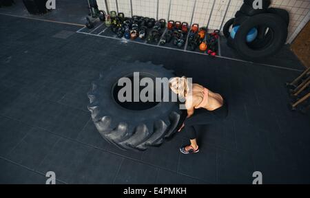 Top view of young female flipping heavy tire. Woman doing crossfit workout at gym. Stock Photo