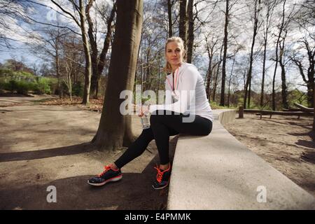 Female runner taking a rest from training in nature. Attractive young woman sitting relaxed with a water bottle. Stock Photo