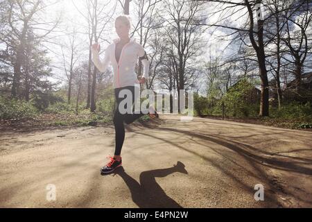 Young caucasian woman running outdoors in forest on a sunny day. Fit female athlete jogging in a park. Caucasian female model tr Stock Photo