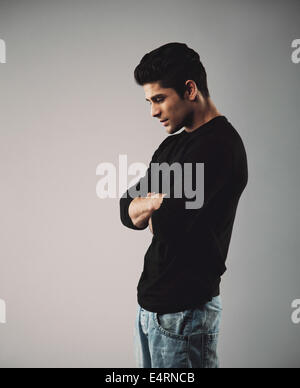 Young man in casuals standing with arms crossed looking down. Male model on grey background. Stock Photo