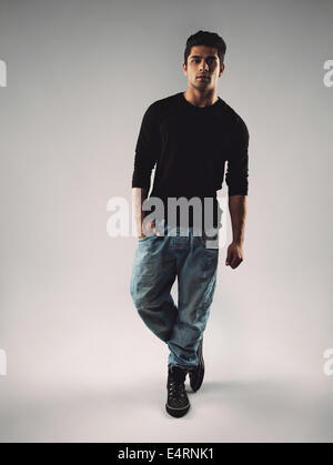 Full length portrait of stylish young man in casuals looking at camera. Hispanic male model posing on grey background. Stock Photo