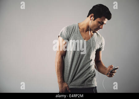 Young hispanic man with cell phone and earphones listening to music on grey background with copy space. Enjoying listening music Stock Photo