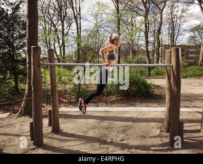 Side view of muscular young woman doing triceps dips on parallel bars at park. Caucasian female fitness model exercising outdoor Stock Photo