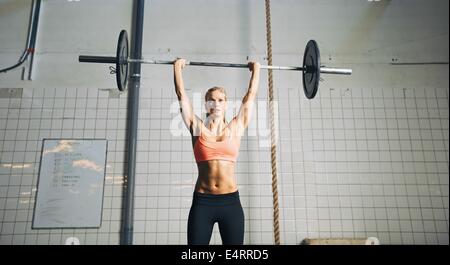 Muscular young female athlete doing weightlifting at crossfit gym. Fit young woman model lifting heavy weights at gym.