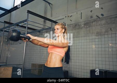 Fitness woman swinging kettle bell at gym. Young caucasian woman doing swing exercise with a kettlebell as a routine of a crossf Stock Photo