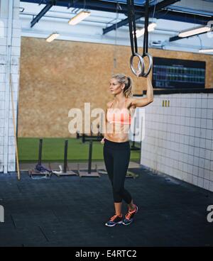 Muscular female athlete holding gymnast rings at the gym. Young caucasian woman exercising at gym with rings. Stock Photo