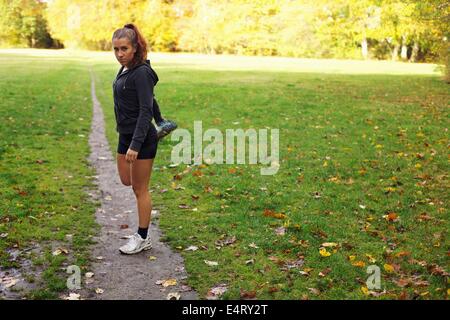 Beautiful young woman stretching leg muscles during workout in park. Pretty young caucasian female runner warming up for a run. Stock Photo