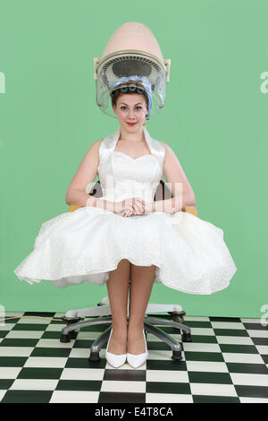 Woman in 1950s style wedding dress sitting under a vintage salon hair drier Stock Photo