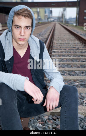 Portrait of teenage boy sitting on railroad tracks, looking at camera, Germany Stock Photo
