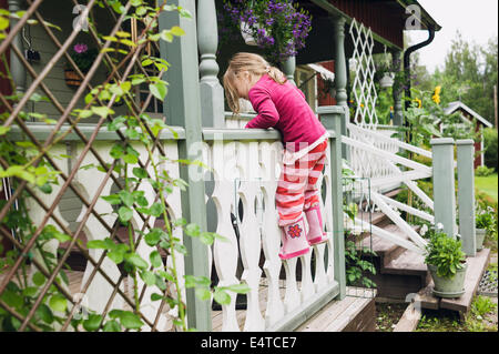 3 year old girl in rubber boots climbing on veranda, Sweden Stock Photo