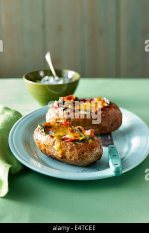 Two stuffed baked potatoes with bacon, spinach, onion and cheddar cheese on a plate on a green tabletop Stock Photo