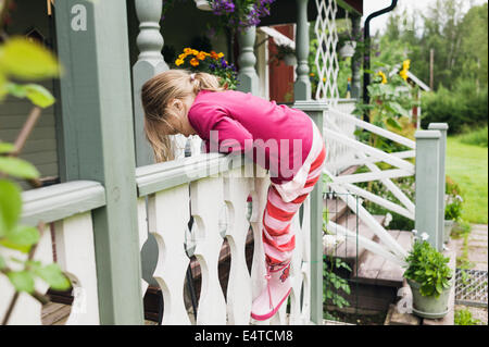 3 year old girl in rubber boots climbs on veranda, Sweden Stock Photo