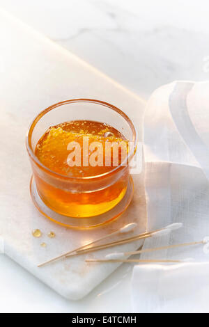 A small glass jar with clear golden honey and a honey comb with cotton swabs. High key image of honey and beauty products. Stock Photo