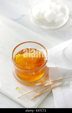 Jar with clear golden honey and a honey comb with cotton swabs and cotton balls. High key image of beauty products Stock Photo