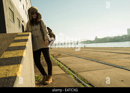 Teenage girl outdoors, wearing trapper hat and sunglasses, standing next to building at loading dock, Mannheim, Germany Stock Photo