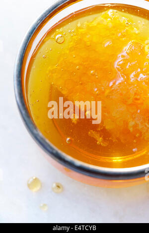Close-up, overhead view of clear golden honey in a glass with a honey comb and air bubbles Stock Photo
