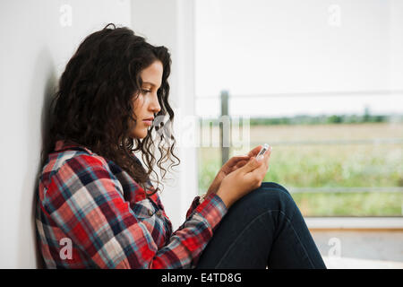 Close-up of teenage girl sitting next to window and using cell phone, Germany
