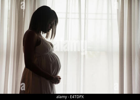 Silhouette of Pregnant Woman Standing by Window Stock Photo