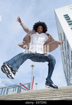 Portrait of young man outdoors, jumping down staircase, looking at camera and smiling, Mannheim, Germany Stock Photo