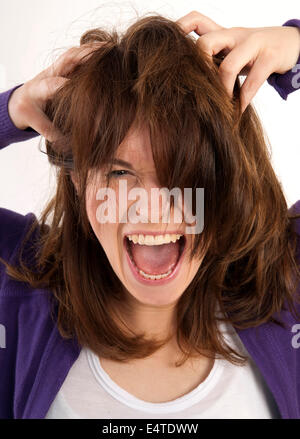 Close-up portrait of young woman screaming and looking at camera with hands in her hair, studio shot on white background Stock Photo