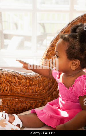 Baby Girl Sitting in Rattan Chair by Window Stock Photo