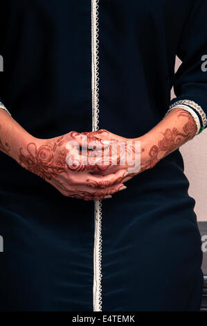 Woman sitting down with close-up of folded hands painted with henna in arabic style, wearing black, arabic, muslim dress Stock Photo