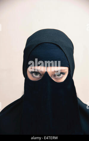 Portrait of young woman in black, muslim hijab and muslim dress, eyes looking at camera with eye makeup, on white background