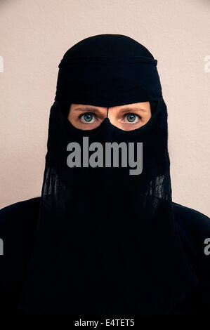 Close-up portrait of woman wearing black muslim hijab and muslim dress, looking at camera, studio shot on white background Stock Photo