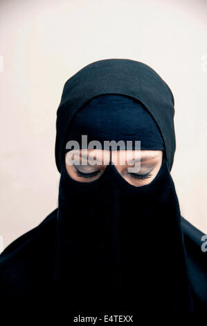 Portrait of young woman in black, muslim hijab and muslim dress, eyes closed with eye makeup, studio shot on white background Stock Photo